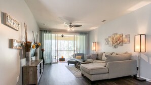 A spacious living room with a large sofa, a coffee table, and a floor lamp. There is a sliding glass door leading to a balcony. - BEAUTIFULLY  CONDO IN LEGENDS GOLF RESORT (Myrtle Beach)
