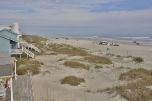 A beach with a building featuring a wooden deck and a staircase leading to a balcony. - Ocean Front Beach Home Walking Distance to Flagler (New Smyrna Beach)