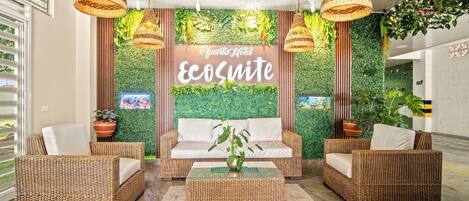 A lobby with wicker furniture, a green wall with plants, and a sign reading "Apartments Hotel Ecosuite".