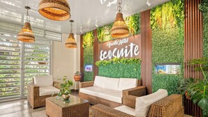 Um hall de hotel moderno com móveis de vime, uma parede verde com plantas e uma placa com a inscrição "Aparto Hotel ecosmite".