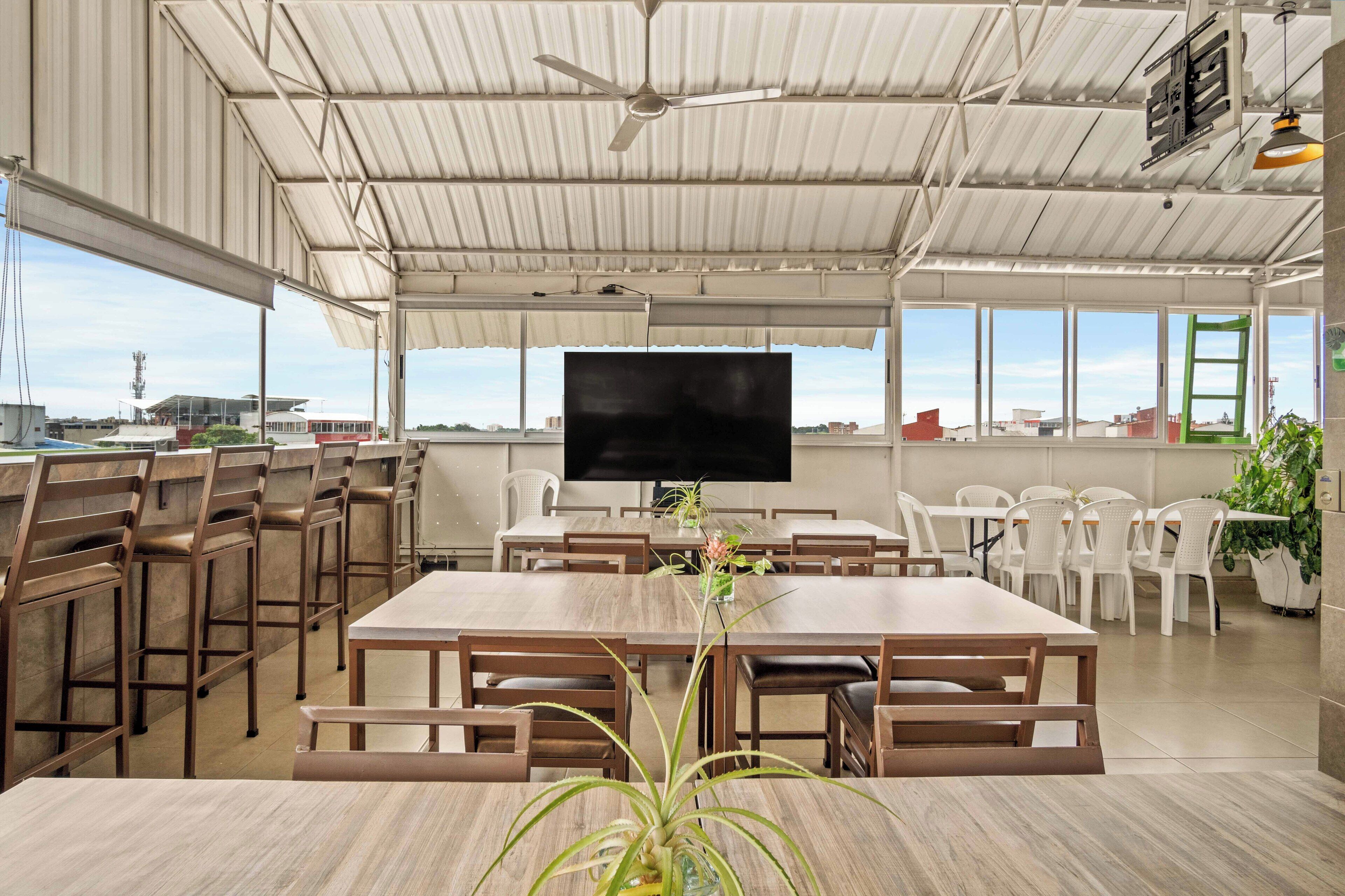 A spacious indoor dining area with high ceilings, a large flat-screen TV, and multiple dining tables and chairs.