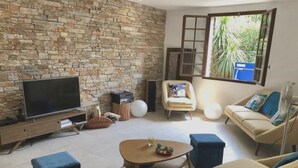Un salon avec un mur en pierre, un téléviseur à écran plat, un canapé, une table basse et un fauteuil.