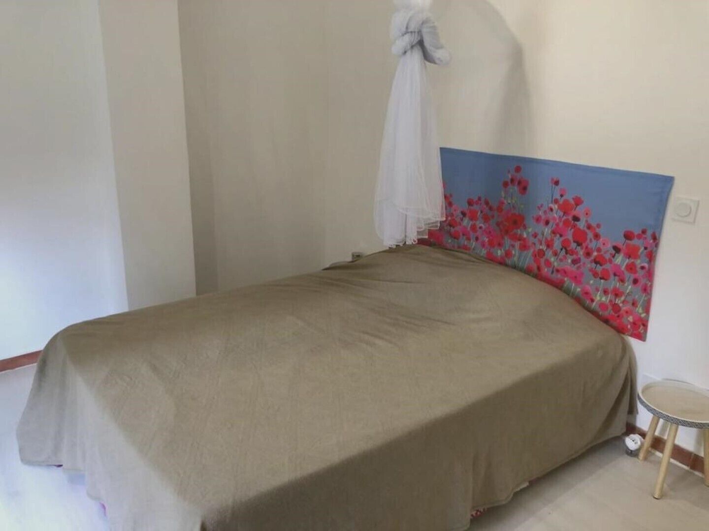 A bedroom with a bed, a white canopy, and a painting of red flowers on the wall.