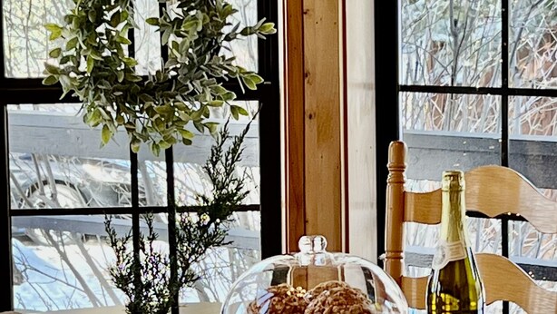 A wooden dining table with a glass dome cover, a bottle of wine, and a potted plant. - Charming Petersen Cottage Rustic Luxury  (Pine Valley)