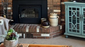 A cozy living room with a brick fireplace, a television mounted on the wall, and a wooden ceiling. - Charming Petersen Cottage Rustic Luxury  (Pine Valley)