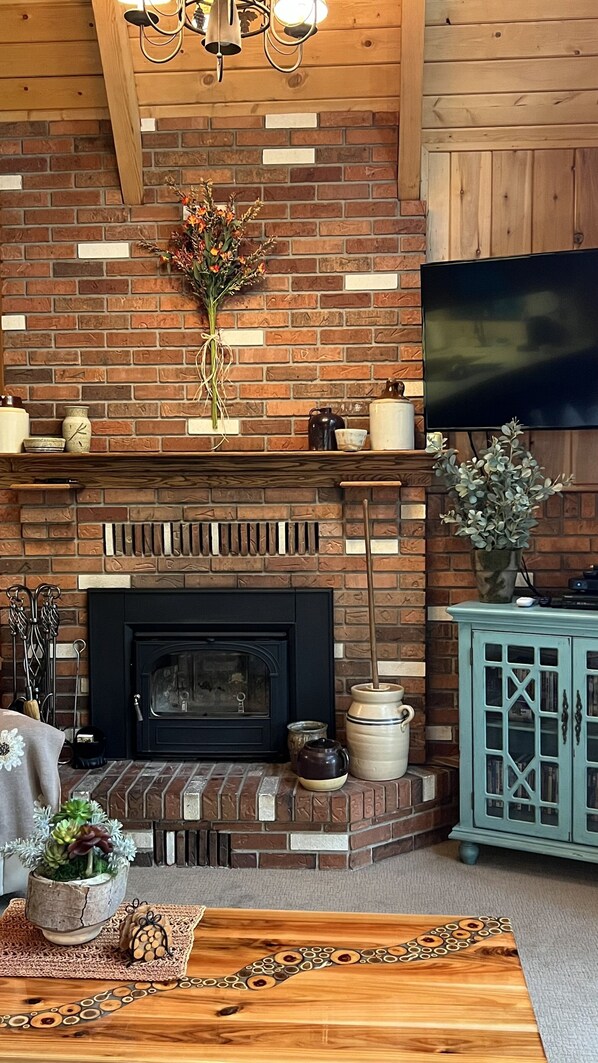A cozy living room with a brick fireplace, a television mounted on the wall, and a wooden ceiling.