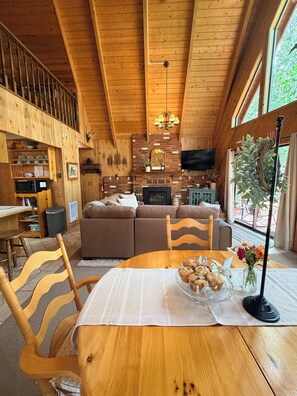 Un interior de madera acogedor con chimenea, televisor y comedor con una mesa dispuesta para una comida.