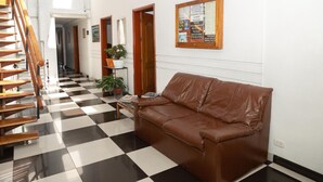 A hotel lobby with a checkered floor, a brown leather sofa, a wooden staircase, and a bulletin board on the wall. - Ayenda 1131 Casa Valencia (Manizales)