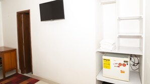 A hallway with a wooden door, a flat-screen TV mounted on the wall, and a white shelf with folded towels and a power strip. - Ayenda 1131 Casa Valencia (Manizales)