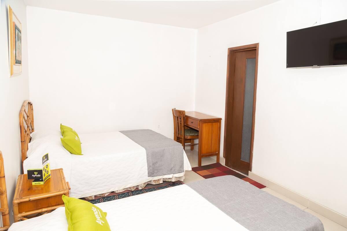 A room with two beds, a desk, a chair, and a television.