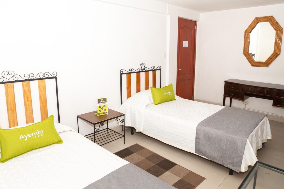 Une chambre d’hôtel avec deux lits, un bureau, un miroir et une porte.