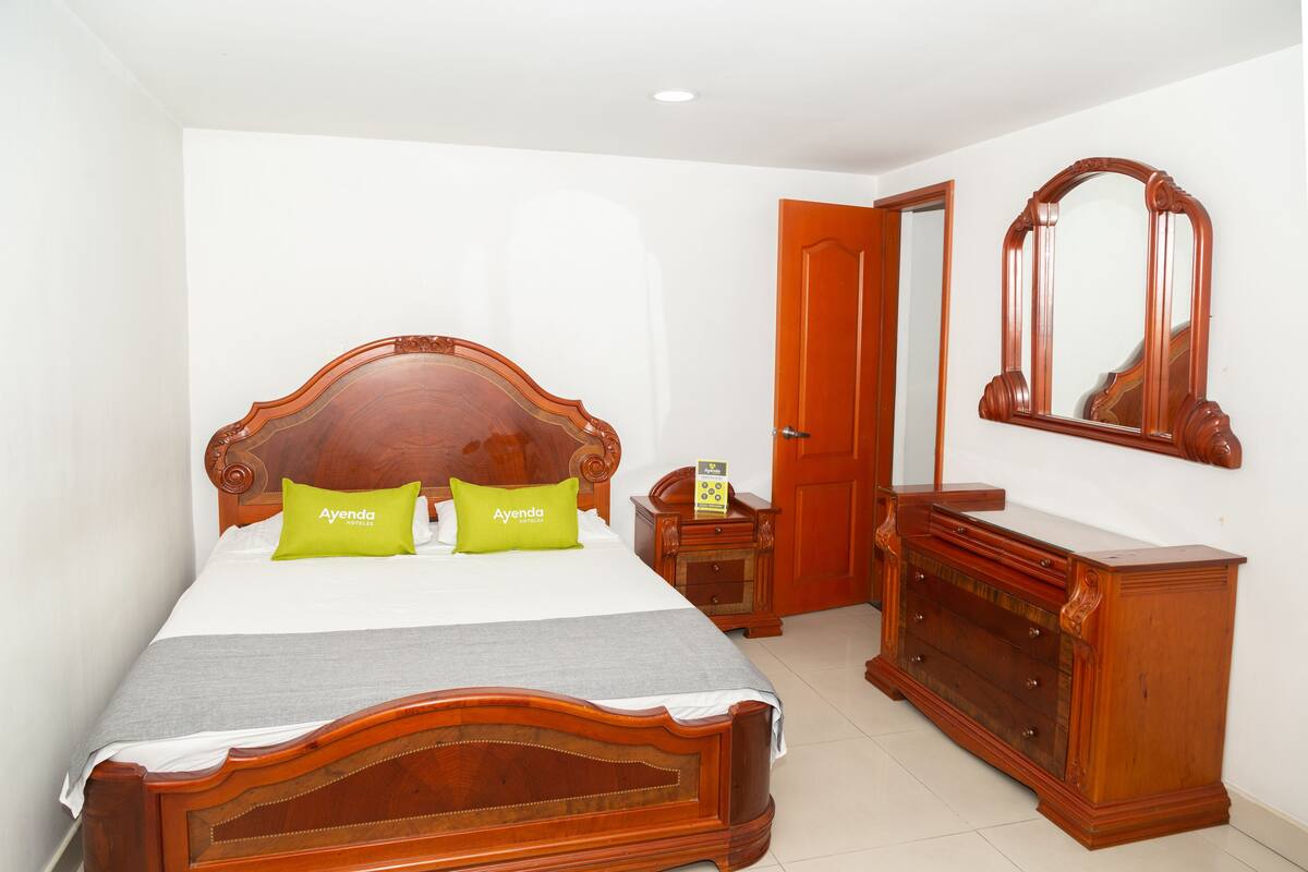 A bedroom with a wooden bed, two green pillows, a wooden dresser, and a mirror on the wall.