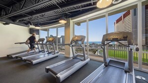 A gym with treadmills, a person using one, large windows, and a view of the ocean.