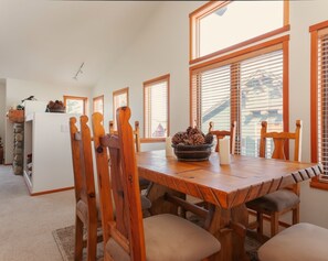 Un coin repas avec une table et des chaises en bois, un mur en pierre et une fenêtre avec des stores.