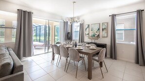 A dining area with a table set for four, surrounded by chairs, and a sofa in the foreground. - 5268OBA: Outdoor Projector 6bed in Solterra minutes from major Orlando attractions (Davenport)