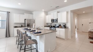 A modern kitchen with white cabinetry, a granite countertop, and a central island with bar stools. - 5268OBA: Outdoor Projector 6bed in Solterra minutes from major Orlando attractions (Davenport)