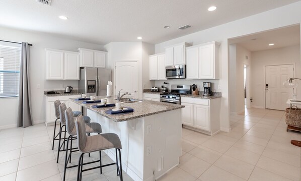 A modern kitchen with white cabinetry, a granite countertop, and a central island with bar stools.