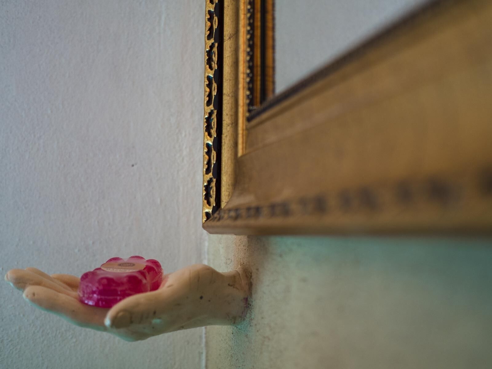 A hand holding a pink object near a corner with a wooden frame.