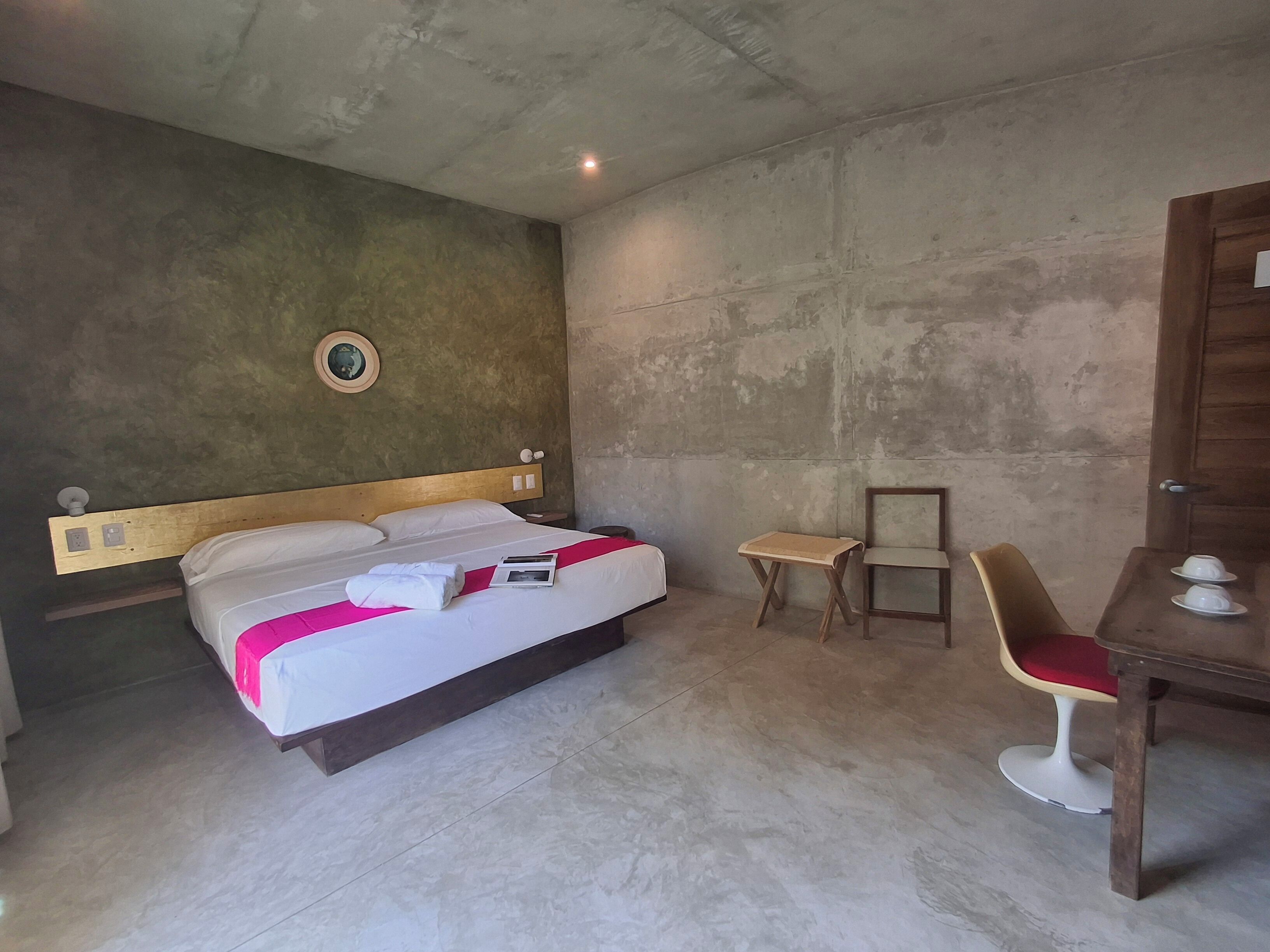 A hotel room with a bed, a small table, a chair, and a wooden wardrobe.