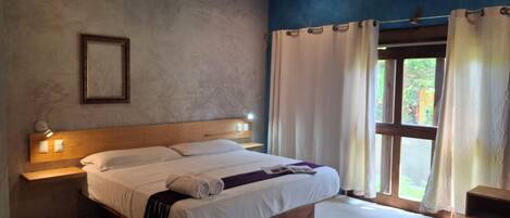 A bedroom with a large bed, bedside lamps, a wooden headboard, a nightstand, a window with curtains, and an air conditioning unit.
