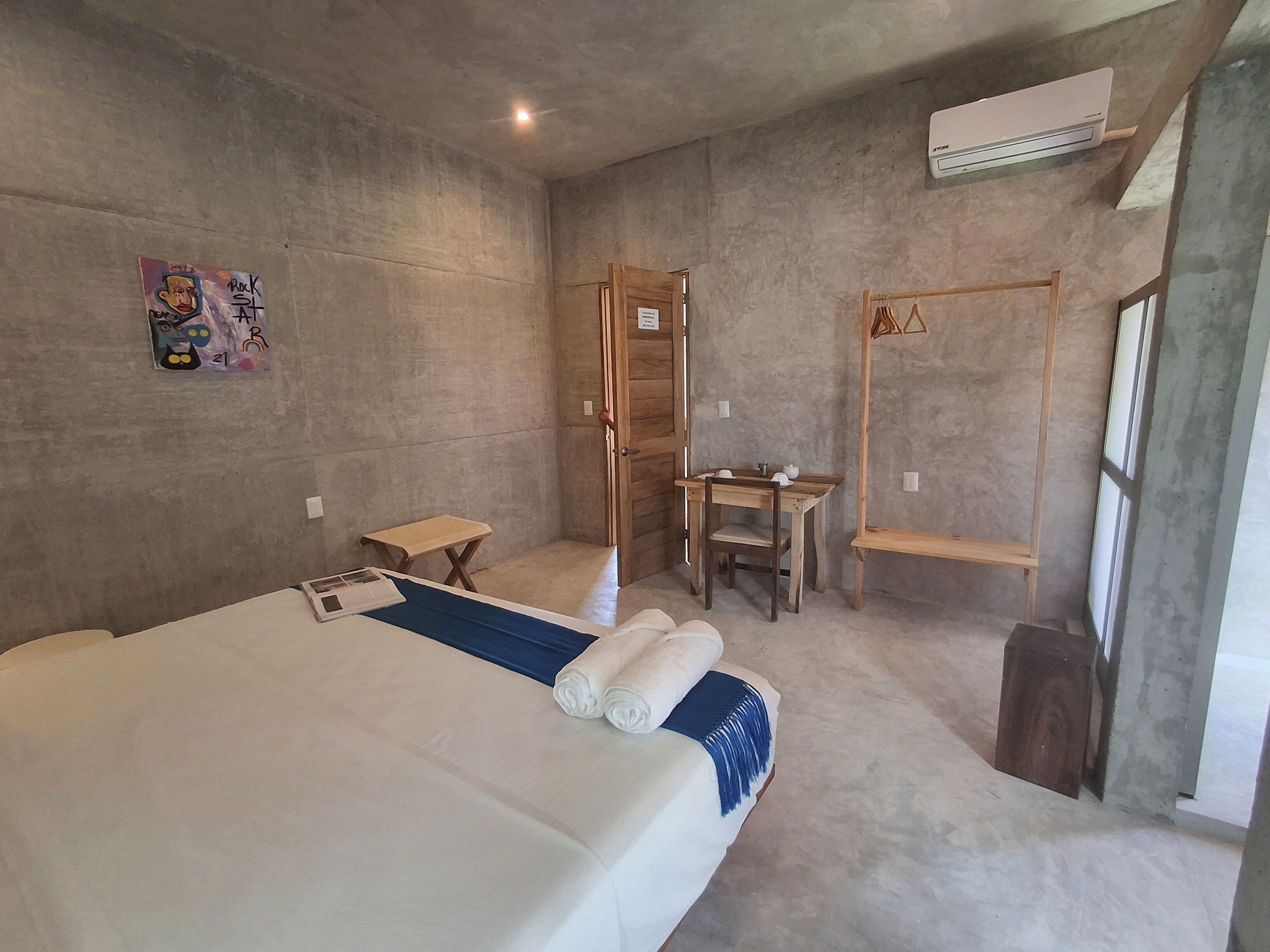 Una habitación con una cama, un escritorio pequeño, una silla y un estante de madera.