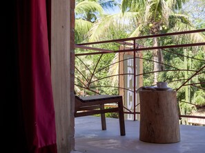 A wooden chair and a small table with a cup and book on a balcony with a view of palm trees and a sign reading "HOTEL".