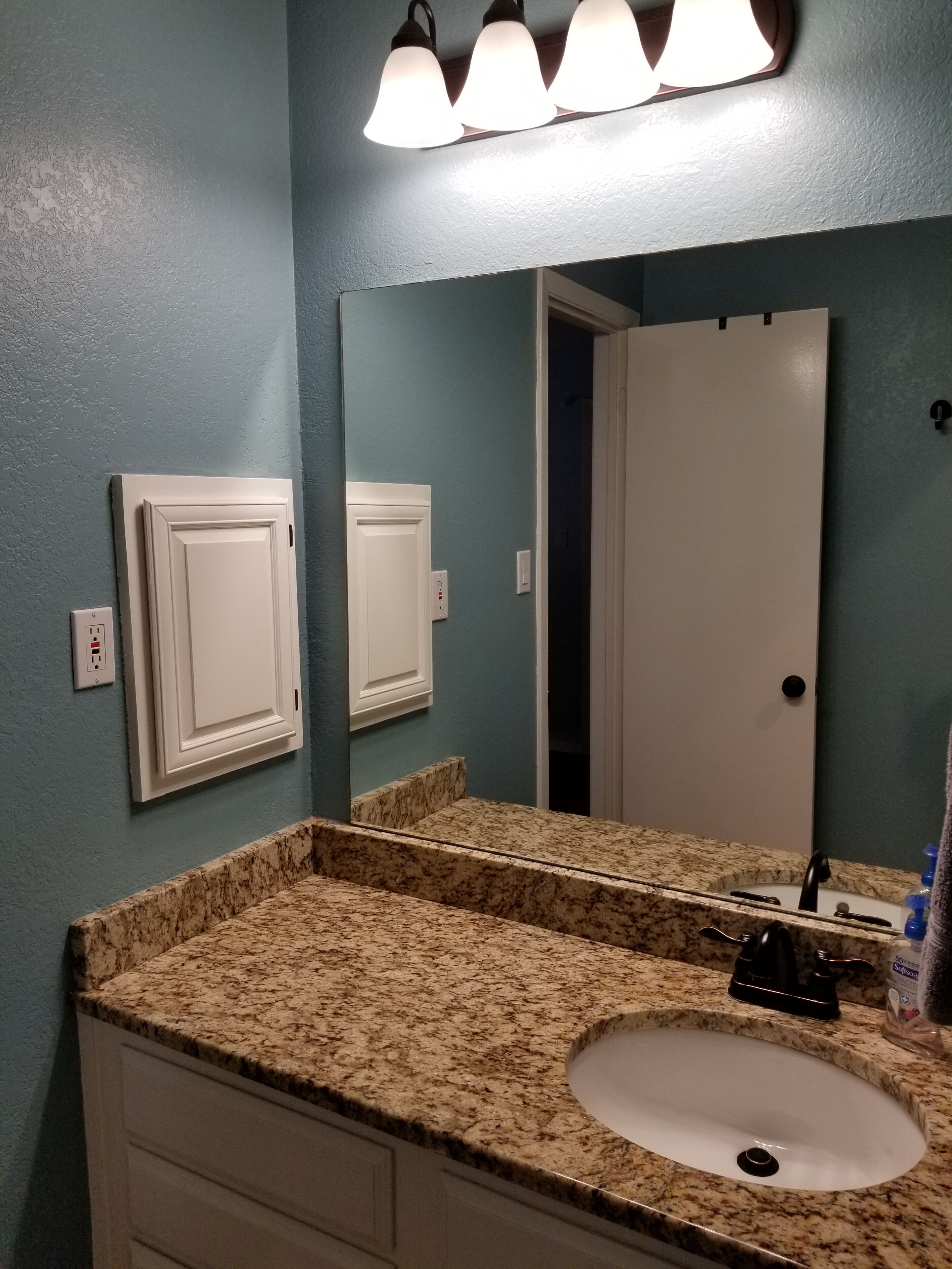 A bathroom with a granite countertop sink, a mirror, and a door.