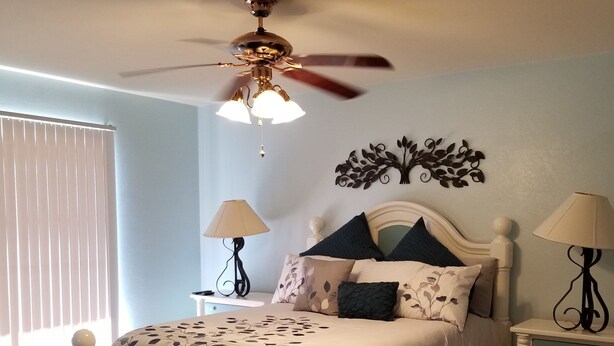 A bedroom with a bed, two nightstands, a ceiling fan, and a decorative wall piece.