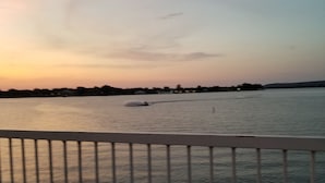 A calm river with a boat in the distance, a railing in the foreground, and a sunset sky. - Hidden Treasure! Charming ground floor condo in waterfront complex. (Marble Falls)