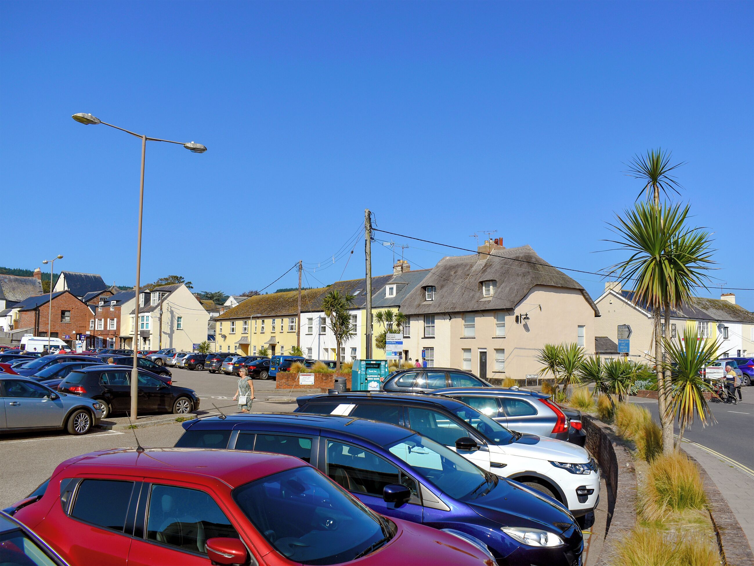 A parking lot with cars, a street, and buildings with thatched roofs.