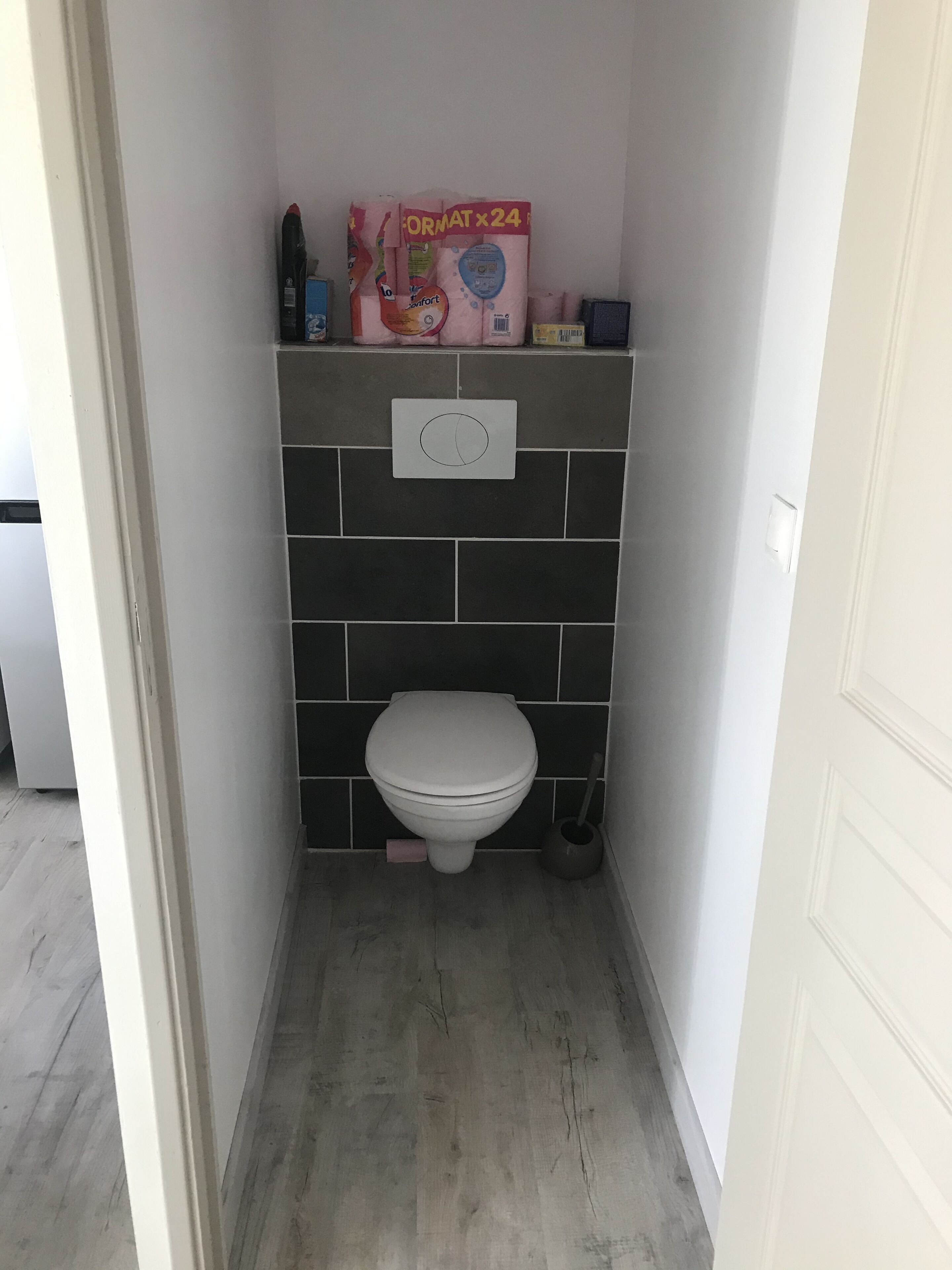Une petite salle de bain comprenant des toilettes, une étagère avec des articles de toilette et un porte-rouleau de papier toilette fixé au mur.