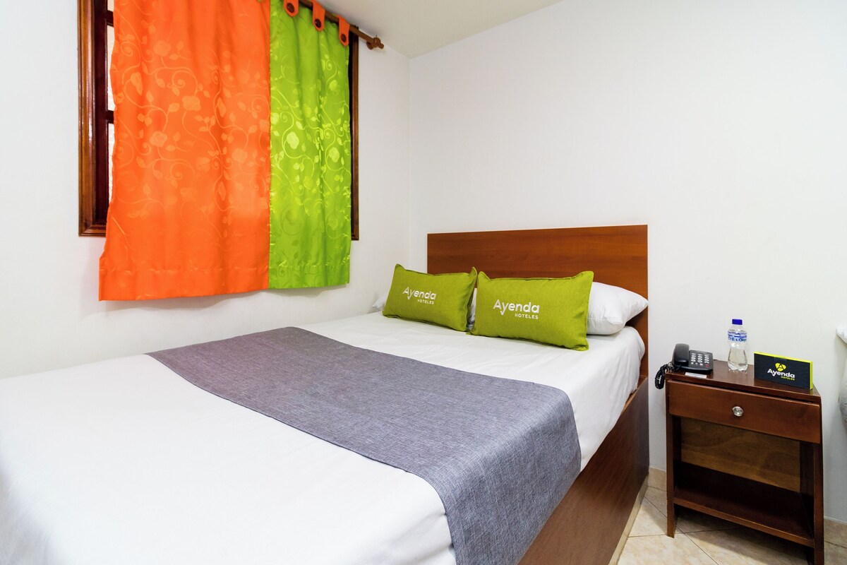 A hotel room with a bed, a nightstand, and a window with curtains.