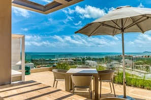 Enjoy unobstructed ocean views from this outdoor terrace with a table and chairs, shaded by a large umbrella.