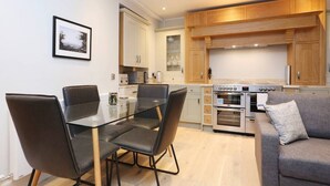 Una cocina moderna con armarios de madera, un comedor con mesa y sillas de vidrio, y un sofá gris.