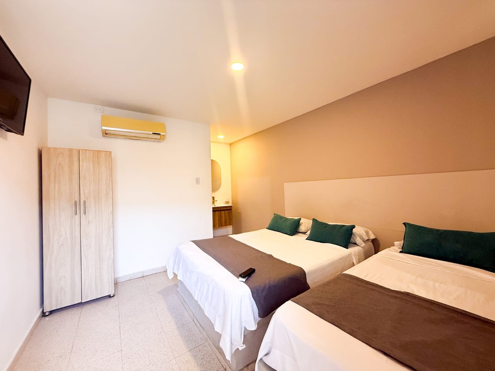 A hotel room with two beds, a wardrobe, and a bathroom visible through an open door.