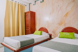 A hotel room with two beds, each with a wooden headboard, a green pillow, and a white bedspread.