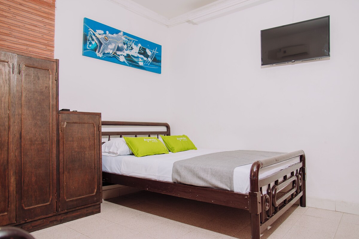 Ein Schlafzimmer mit einem hölzernen Bett, einem Kleiderschrank, einem Flachbildfernseher und einem blauen, abstrakten Gemälde an der Wand.