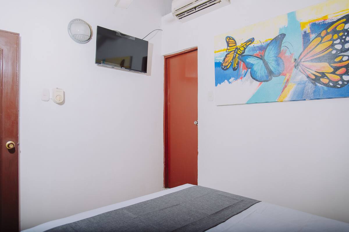 Ein Schlafzimmer mit einem Bett, einem an der Wand montierten Fernseher, einer roten Tür und einem farbenfrohen Schmetterlingsbild.