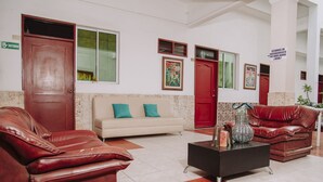 Un vestíbulo con un sofá beige, sofás de cuero rojo, una mesa de centro negra y una puerta roja.