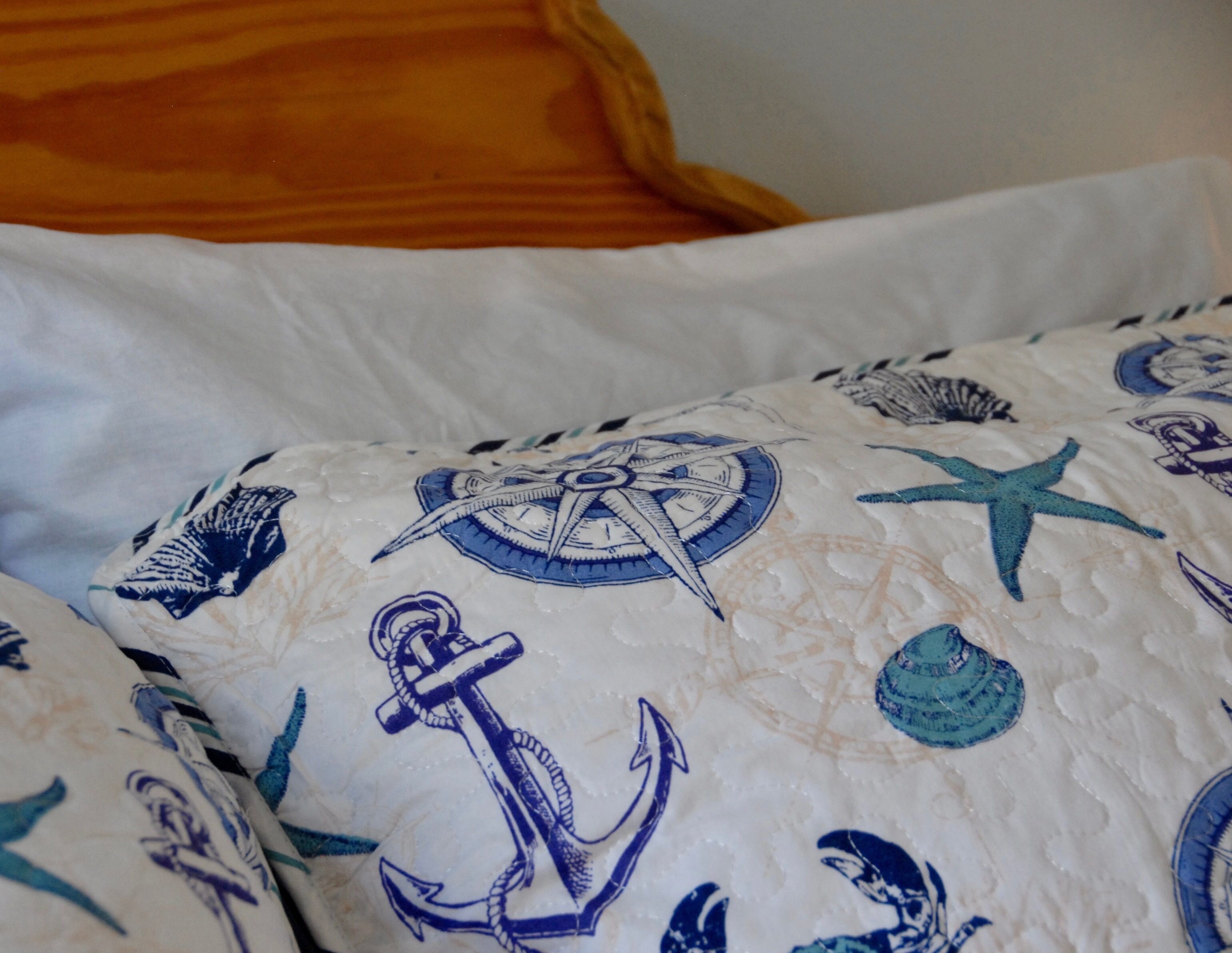 A bed with a nautical-themed duvet cover featuring anchors, a compass, and starfish.