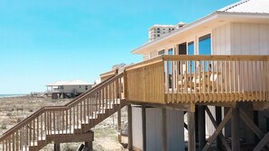 A beachfront house with a wooden deck and a staircase leading to a covered area. - Beach House - Gulf Front!  Right on the Beach! - WIFI - Sleeps 10- Pools (Gulf shores)