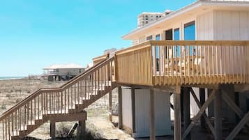 Una casa frente a la playa con un balcón de madera y una escalera que conduce a un espacio cubierto.