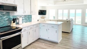 A modern kitchen with white cabinets, a black stove, and a blue-tiled backsplash. - Beach House - Gulf Front!  Right on the Beach! - WIFI - Sleeps 10- Pools (Gulf shores)