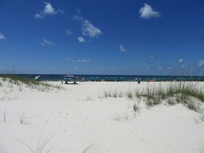 Een strand met wit zand, enkele parasols en een helderblauwe lucht.