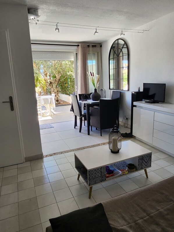 A modern living room with a dining area, a TV, and a view of the outdoors. - Private residence with swimming pool, private parking, 4-room apartment on the ground floor. (CAP-Agde)