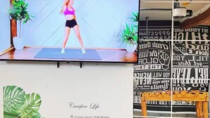 A television displaying a fitness video, a wooden floor, a potted plant, and a wall with motivational text.