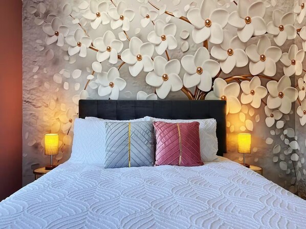 Una cama con cubrecolcha blanco acolchado, dos lámparas de noche y una pared con estampado floral.