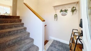 A staircase with carpeted steps, a wooden handrail, and a wall-mounted sign with hanging plants.