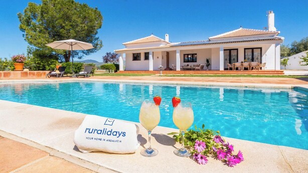 Blick auf ein Haus mit Pool, zwei Gläser mit Getränken und ein Handtuch mit Aufschrift.