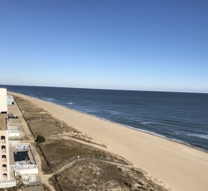 A beach with a sandy shore, a clear blue sky, and a building with a balcony and outdoor seating area. - 1 Bedroom Condo with Ocean View in beach block (Ocean City)